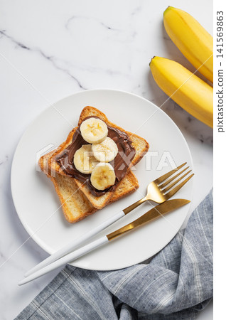 Toasted bread with chocolate cream and banana on a plate on a marble background 141569863