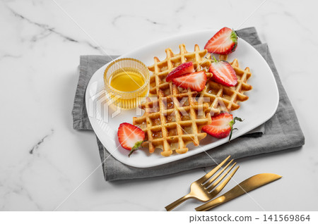 Belgian waffles with fresh strawberries and honey on a white plate on  a marble background 141569864