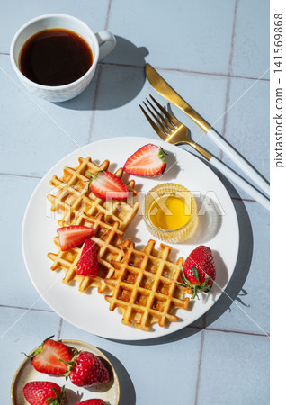 Belgian waffles with fresh strawberries and honey on a white plate on  a blue tile background 141569868