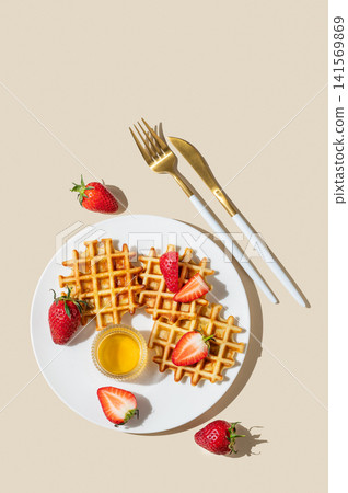 Belgian waffles with fresh strawberries and honey on a white plate on a yellow background Belgian waffles with fresh strawberries and honey on a white plate on a yellow background 141569869