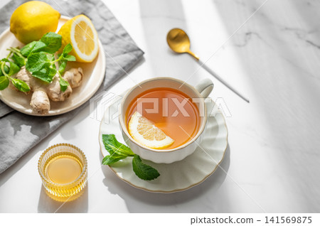 Cup of tea with lemon, ginger, honey and mint on a marble background with citrus fruits Cup of tea with lemon, ginger, honey and mint on a marble background with citrus fruits 141569875