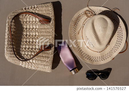 Flat Lay of Beach Accessories Woven Straw Bag Hat Sunglasses and Cosmetics Tube 141570327