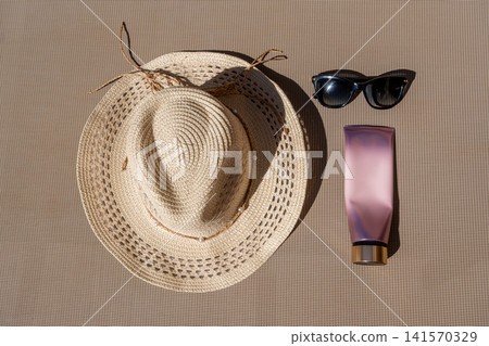 Flat Lay of Summer Essentials Straw Hat Sunglasses and Cosmetic Tube 141570329