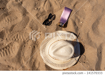Flat Lay of Summer Sun Protection Essentials Straw Hat Sunglasses and Cream Tube on Sand Flat Lay of Summer Sun Protection Essentials Straw Hat Sunglasses and Cream Tube on Sand 141570333
