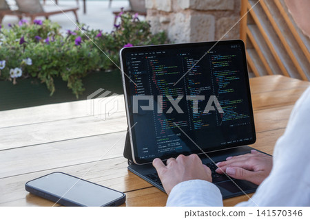 Over Shoulder View of Software Developer Coding on Tablet at Outdoor Cafe Over Shoulder View of Software Developer Coding on Tablet at Outdoor Cafe 141570346