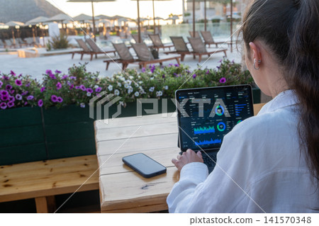 Over Shoulder View of Woman Analyzing Financial Charts on Tablet at Resort Cafe Over Shoulder View of Woman Analyzing Financial Charts on Tablet at Resort Cafe 141570348