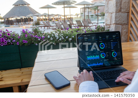 Business Analytics Dashboard on Tablet Screen at Outdoor Resort Terrace Business Analytics Dashboard on Tablet Screen at Outdoor Resort Terrace 141570350