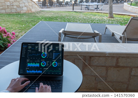 Hands Typing on Tablet with Financial Dashboard at Resort Outdoor Terrace 141570360