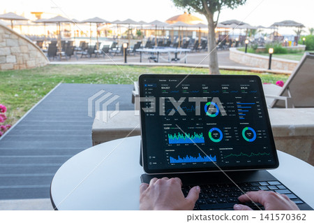 Hands Typing on Tablet with Financial Dashboard at Resort Outdoor Terrace 141570362