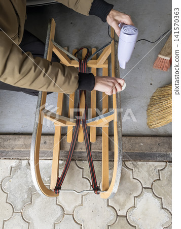 Father Maintaining a Wooden Sled for His Child 141570363