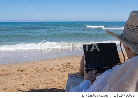 Over Shoulder View of Woman Reviewing Business Dashboard on Beach Lounge Chair Over Shoulder View of Woman Reviewing Business Dashboard on Beach Lounge Chair 141570366