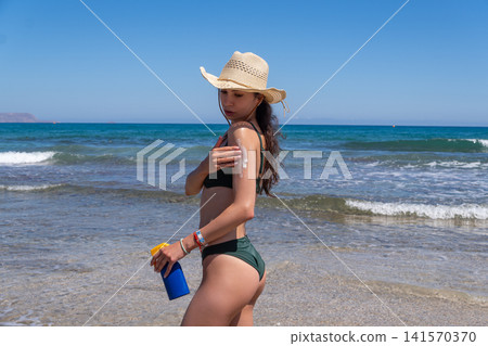 Young Brunette Woman Rubbing Sun Protection Cream on Shoulder at Seashore Young Brunette Woman Rubbing Sun Protection Cream on Shoulder at Seashore 141570370