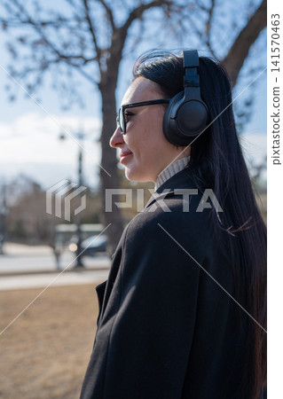 One young girl in park listening to music on wireless headphones and using her phone One young girl in park listening to music on wireless headphones and using her phone 141570463