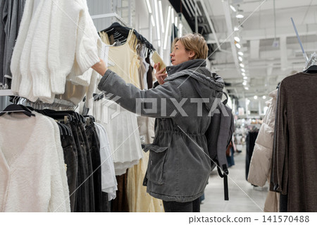 Young woman buying new clothes in store. Sale shopping fashion and people concept Stock Photo Young woman buying new clothes in store. Sale shopping fashion and people concept Stock Photo 141570488