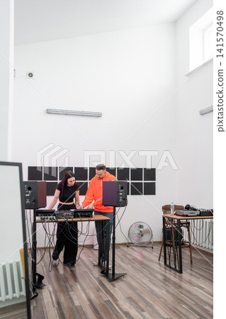 Female DJ practicing electronic music mixing at studio desk with instructor watching closely. DJ, practice, music, studio, instructor Female DJ practicing electronic music mixing at studio desk with instructor watching closely. DJ, practice, music, studio, instructor 141570498