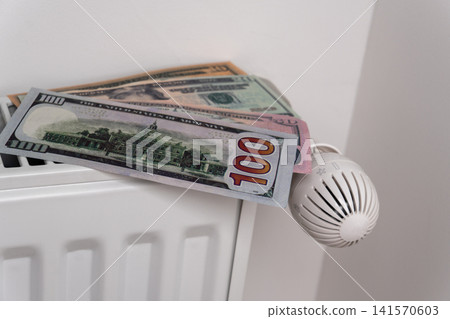 US dollar banknotes on central heating radiator with thermostat valve US dollar banknotes on central heating radiator with thermostat valve 141570603
