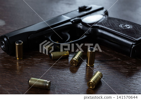Black semi automatic pistol with rubber bullet cartridges on wooden table 141570644
