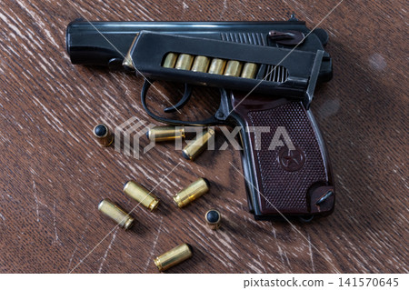 Handgun with loaded magazine and scattered rubber bullet cartridges on wooden background 141570645
