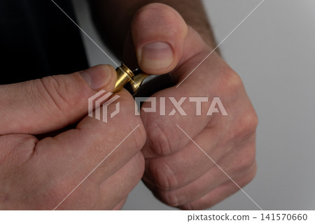 Detailed view of man inserting ammunition cartridge into handgun magazine Detailed view of man inserting ammunition cartridge into handgun magazine 141570660