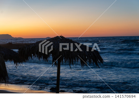 Thatch beach umbrella silhouette against colorful sunset sea Thatch beach umbrella silhouette against colorful sunset sea 141570694