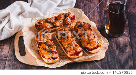 Baked hot dog buns with cheese, sausages, tomatoes and herbs on paper on the table web banner Baked hot dog buns with cheese, sausages, tomatoes and herbs on paper on the table web banner 141570835