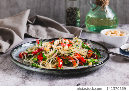 A delicious salad of glass noodles, fried bell peppers, cilantro, and nuts on a plate on the table A delicious salad of glass noodles, fried bell peppers, cilantro, and nuts on a plate on the table 141570869
