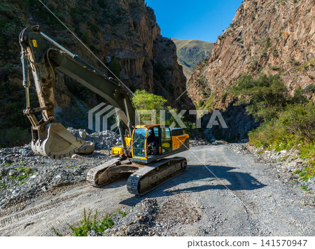 Excavator Working on Gravel Road in Mountain Gorge Excavator Working on Gravel Road in Mountain Gorge 141570947