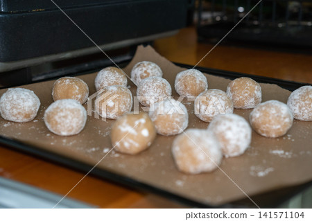 Homemade almond cookies prepared on baking tray with powdered sugar coating before baking. Home baking, dessert preparation, recipe, confectionery, family cooking, homemade food 141571104