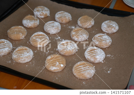 Tray filled with homemade almond cookies ready for baking after shaping and coating with powdered sugar. Home baking, dessert, recipe, family tradition, cooking, confectionery 141571107