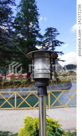 Close-up of ornate black metal lamp post with a yellow metal railing and red-roofed cabins, tourism concept. 141571156