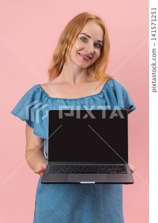 Smiling woman holding a modern laptop with a blank screen, presenting or displaying online content or a product against a vibrant pink background for copy space Smiling woman holding a modern laptop with a blank screen, presenting or displaying online content or a product against a vibrant pink background for copy space 141571251