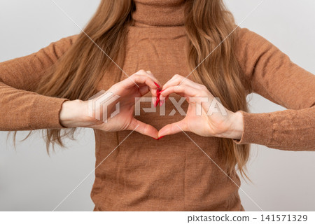 Woman forming a heart with hands close to chest, conveying love, support, kindness and gratitude, warm, intimate gesture symbolizing connection, well being and empathy Woman forming a heart with hands close to chest, conveying love, support, kindness and gratitude, warm, intimate gesture symbolizing connection, well being and empathy 141571329