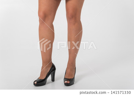 Woman's lower body posed on white background highlighting elegant legs and black patent leather platform peep toe heels for a sophisticated, fashion forward studio look Woman's lower body posed on white background highlighting elegant legs and black patent leather platform peep toe heels for a sophisticated, fashion forward studio look 141571330