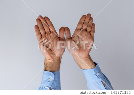 Human hands in a light blue dress shirt creating an open gesture against a simple background, symbolizing concepts of invitation, freedom, or protection 141571333