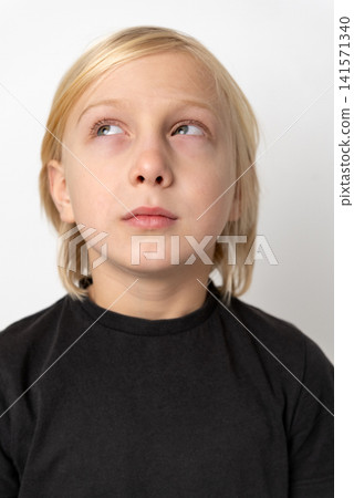 Young blonde boy looking up and to the side with a pensive expression, representing concepts of thinking, imagination, curiosity, and concentration on a plain white background 141571340