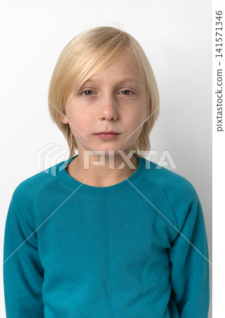 Young boy with blonde hair and light colored eyes posing in a teal long sleeve shirt, looking directly at the camera with a serious expression against a white studio background Young boy with blonde hair and light colored eyes posing in a teal long sleeve shirt, looking directly at the camera with a serious expression against a white studio background 141571346
