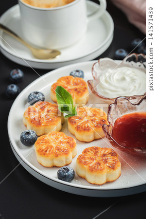 Cottage cheese pancakes, syrniki, curd fritters decorated with strawberry and raspberry served on a white plate. Homemade breakfast concept Cottage cheese pancakes, syrniki, curd fritters decorated with strawberry and raspberry served on a white plate. Homemade breakfast concept 141571439