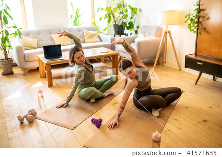Athletic personal trainer and mature female client bending sideways Athletic personal trainer and mature female client bending sideways 141571635