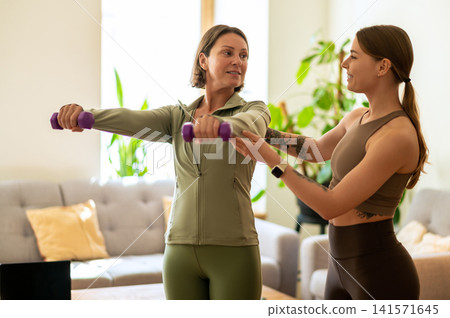 Fitness instructor adjusting arm position of mature woman Fitness instructor adjusting arm position of mature woman 141571645