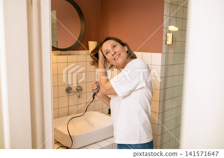 Middle aged woman drying her hair with hairdryer 141571647