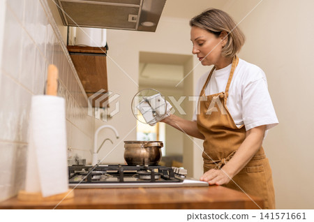 Middle aged woman lifting pot lid with towel Middle aged woman lifting pot lid with towel 141571661