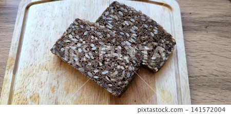 Two slices of dark, seeded whole grain bread resting on a light wooden cutting board Two slices of dark, seeded whole grain bread resting on a light wooden cutting board 141572004