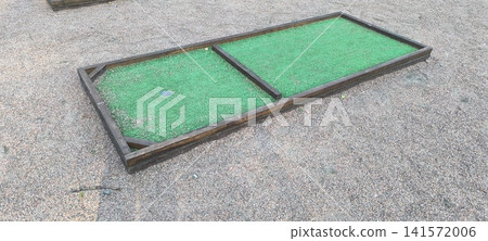 rectangular outdoor mini-golf putting green framed with wood and featuring green artificial turf and a metal hole rectangular outdoor mini-golf putting green framed with wood and featuring green artificial turf and a metal hole 141572006