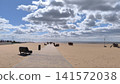 wide sandy beach with a paved promenade leading towards the ocean under a blue sky with fluffy white clouds 141572038