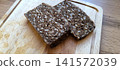 Two slices of dark, seeded whole grain bread resting on a light wooden cutting board 141572039