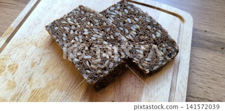 Two slices of dark, seeded whole grain bread resting on a light wooden cutting board Two slices of dark, seeded whole grain bread resting on a light wooden cutting board 141572039