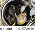 top-down view of stainless steel kitchen sink filled with very dirty dishes, including frying pan with food residue, fork, ceramic bowls with dried stains 141572040