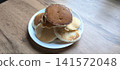 white ceramic plate piled with golden-brown fluffy homemade pancakes, captured in natural lighting on a light wood grain table surface 141572048