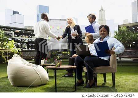 African american woman reviewing clipboard notes beside laptop on urban office terrace, work from anywhere concept. Businesswoman reading data from files. 141572424