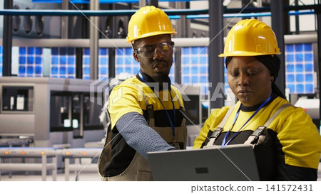 Solar panels plant engineering team using laptop to oversee machinery systems. Photovoltaics plant teamworking colleagues use software on notebook to maintain operations, camera A Solar panels plant engineering team using laptop to oversee machinery systems. Photovoltaics plant teamworking colleagues use software on notebook to maintain operations, camera A 141572431